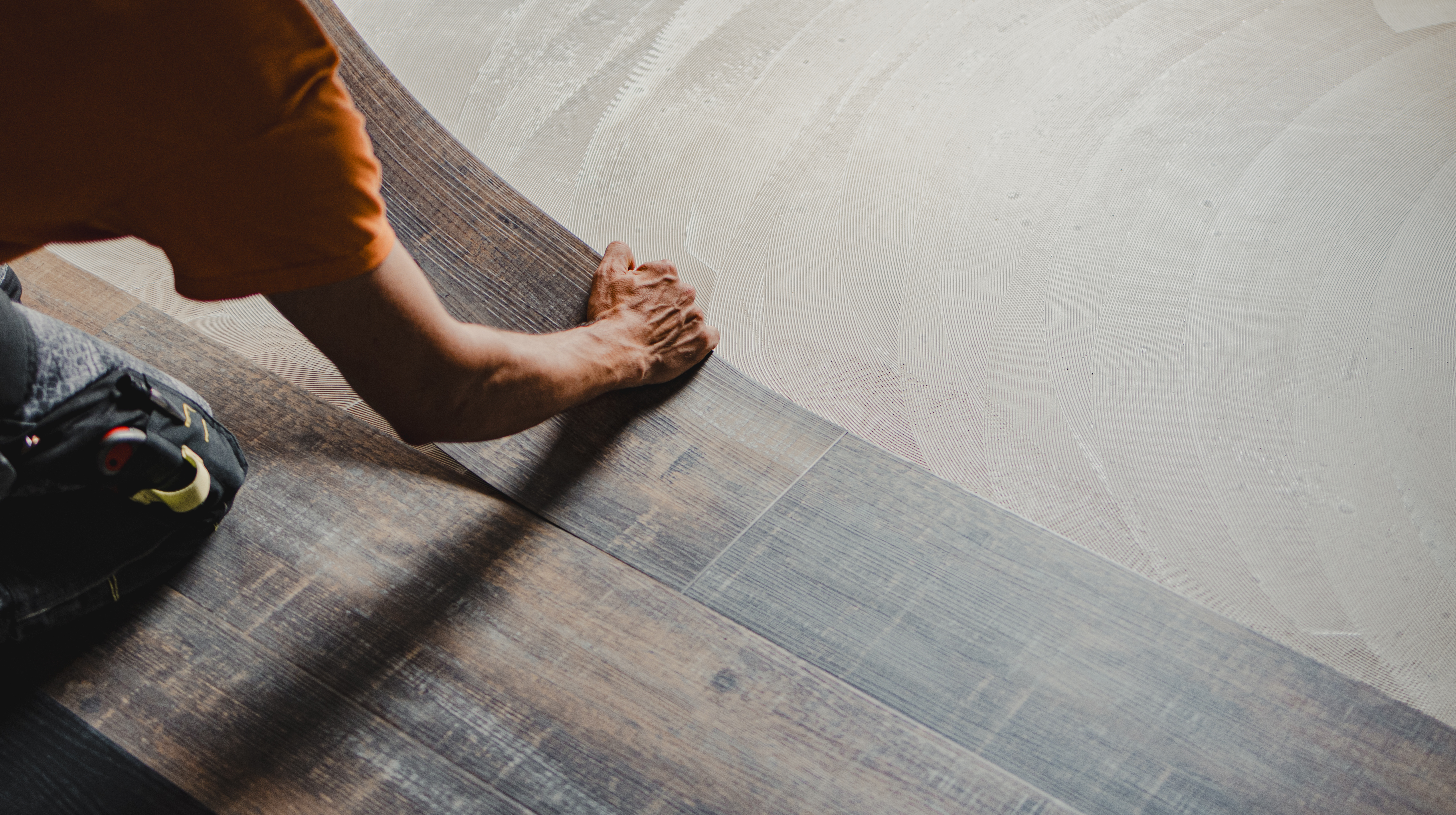 Construction worker installing luxury vinyl plank flooring using glue down method