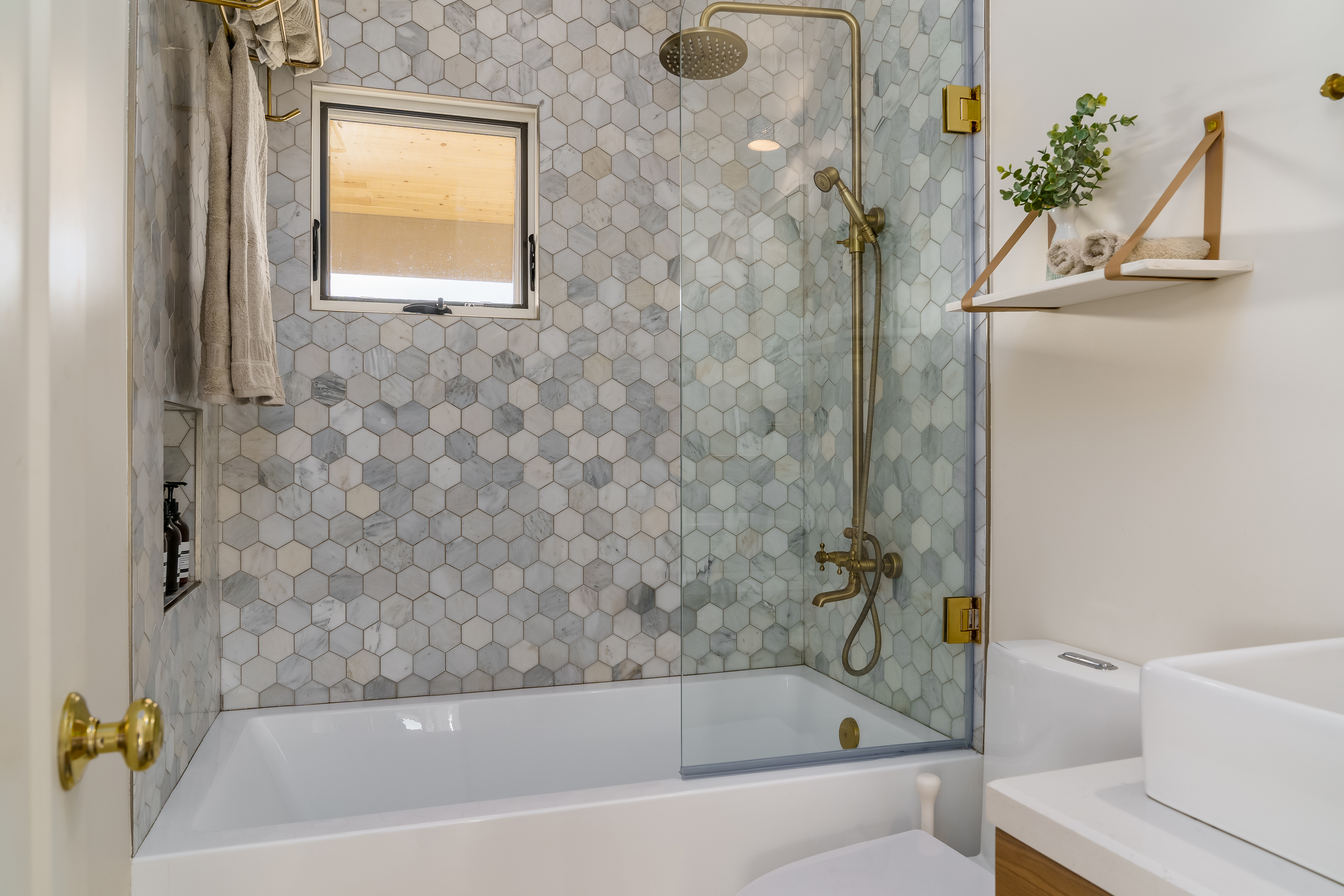 Modern bathroom in white with shower tub with hexagonal tile and gold brass fixtures